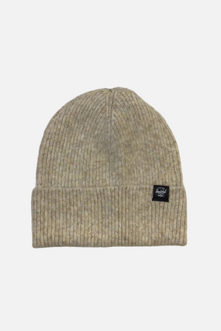 A light beige ribbed knit beanie hat with a small black brand patch on the front cuff, photographed against a plain off-white background.