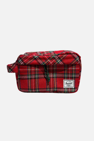 A red plaid Herschel toiletry bag with a black drawstring and a white brand patch, displayed on a white shelf.